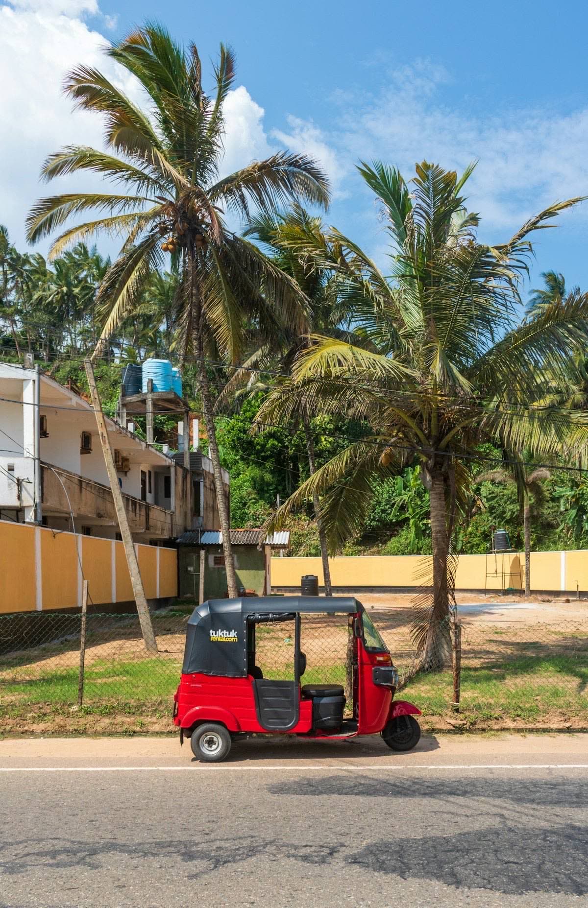 A classic red Sri Lankan tuk-tuk pulled up on a palm-lined south-coast road