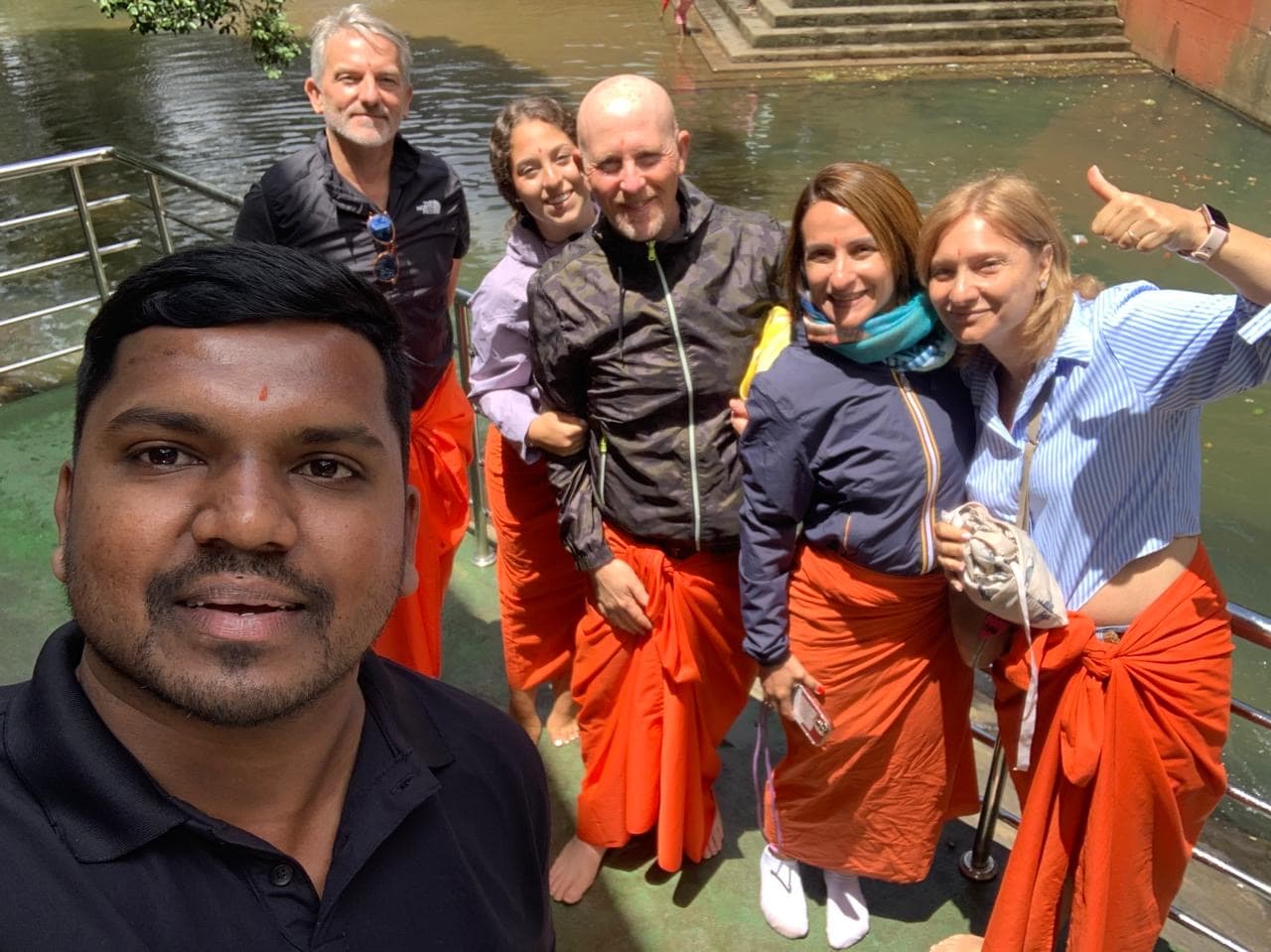 Tour guide and five guests in orange temple sarongs standing beside a sacred pool